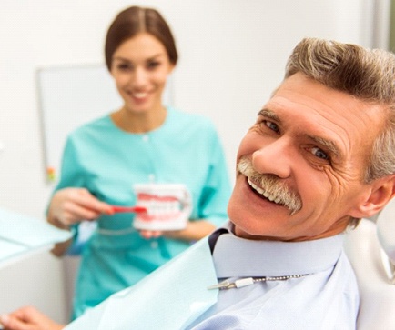 man smiling in dental chair with dental assistant in the room
